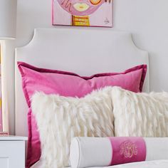 a white bed topped with pink pillows next to a painting