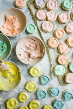 colorful cupcakes and icing on a marble table with bowls of frosting