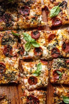 several slices of pizza with basil and pepperoni on top, sitting on a wooden cutting board