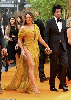 a woman in a yellow dress walking down the red carpet with two men behind her