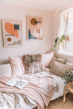 a bed with pillows and blankets in a bedroom next to a window filled with potted plants