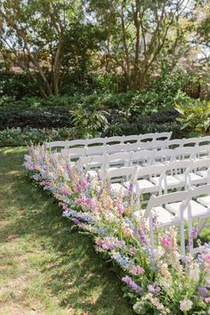 an outdoor ceremony setup with white chairs and purple flowers on the grass, surrounded by trees