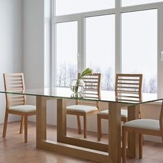 a glass dining table with four chairs and a vase on the end, in front of large windows