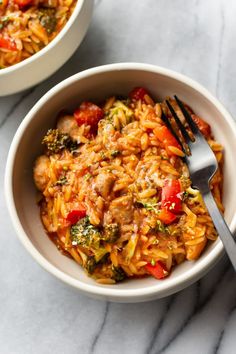 two bowls filled with pasta and vegetables on top of a marble counter next to a fork