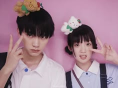 two young people standing next to each other in front of a pink wall with teddy bears on their heads