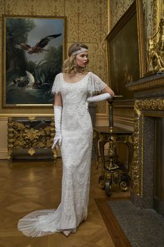 a woman standing in front of a painting wearing white gloves and a dress with sheer sleeves