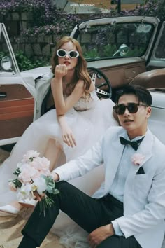 a man and woman sitting next to each other in front of a car with flowers