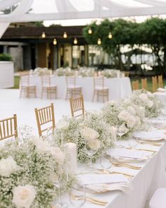 a long table is set with white flowers and gold place settings for an outdoor wedding