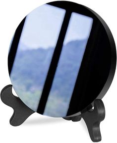 a round mirror sitting on top of a black stand with mountains in the back ground