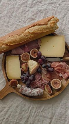 an assortment of cheeses, meats and fruit on a wooden platter with a knife