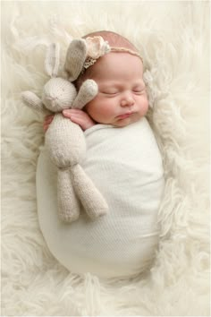 a baby sleeping with a stuffed animal on top of it's back in a white blanket