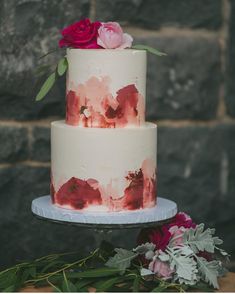 a three tiered cake with pink flowers on top and white icing, sitting on a plate