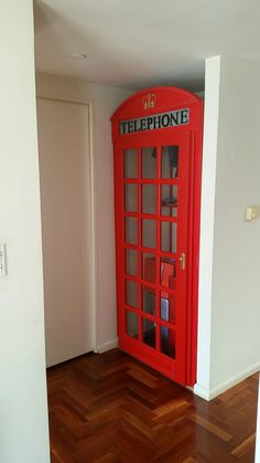 a red phone booth sitting on top of a hard wood floor next to a white wall