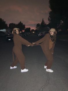 two people in costumes holding hands while standing on the street at night with cars behind them