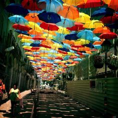 many colorful umbrellas are hanging from the ceiling in an alleyway with people walking under them