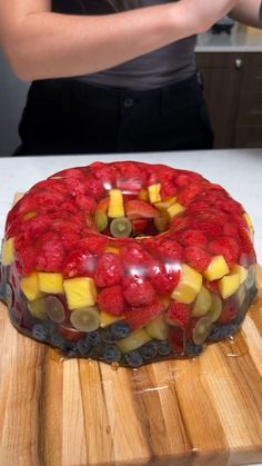 a woman standing in front of a cake on top of a wooden cutting board with fruit