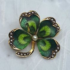 The Krementz Art Nouveau 1900 Clover Enameled Brooch is a fine example of early 20th-century craftsmanship. This brooch, made by the renowned American jewelry firm Krementz & Co., exemplifies the Art Nouveau style with its intricate design and nature-inspired motifs. Crafted in 14Kt gold, the brooch features a delicate clover design, which is a common symbol in Art Nouveau jewelry, representing nature's beauty and the movement's fascination with organic forms. The leaves of the clover are beauti Art Deco Yellow Gold Collectible Brooches, Art Nouveau Enamel Brooch Jewelry, Yellow Gold Enamel Brooches Hallmarked, Gold Enamel Art Nouveau Brooches, Elegant Enamel Brooch Pin, Art Nouveau Yellow Gold Collectible Brooches, Antique Enamel Brooches For Formal Occasions, Victorian Style Enamel Pin Gift, Yellow Gold Enamel Brooches For Gifts