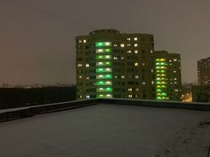 an apartment building is lit up with green lights in the snow at night on a cloudy day