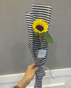 a person holding a sunflower wrapped in black and white paper with a name tag