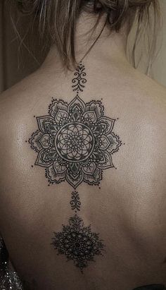 the back of a woman's neck with an intricate tattoo design on her left shoulder