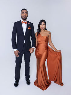 a man in a tuxedo standing next to a woman in an orange dress