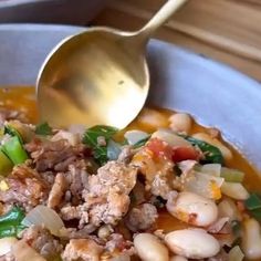 a white bowl filled with meat, beans and greens next to a gold ladle