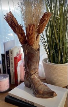 a pair of boots sitting on top of a book next to a potted plant