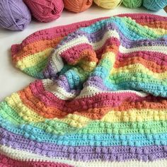 a crocheted blanket with balls of yarn in the background