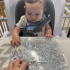 a baby sitting in a highchair and looking at something on the table with it's hands