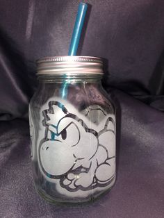 a glass jar with a blue straw sticking out of it's mouth and cartoon character drawn on the lid