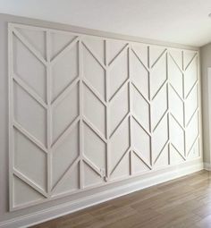 an empty room with white walls and wood flooring in the center, there is a large paneled wall that has geometric designs on it