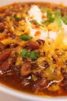 a white bowl filled with chili and beans covered in sour cream, cheese and green onions