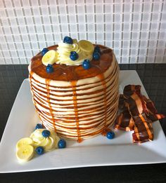 a stack of pancakes with blueberries, bananas and syrup on a white platter