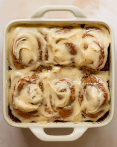 a white casserole dish filled with cinnamon rolls covered in cream cheese icing