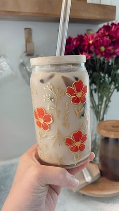 a hand holding a glass with flowers painted on it and a straw in the cup