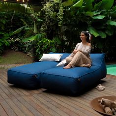 a woman sitting on top of a blue couch next to a pool in the middle of a wooden deck