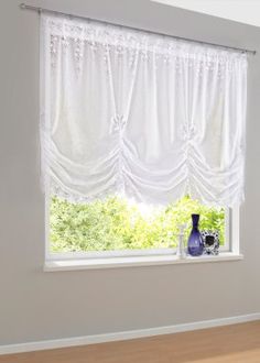 a window with white curtains and a vase in front of it on a wooden floor