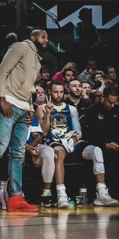 a man standing on top of a basketball court next to another man sitting in front of him