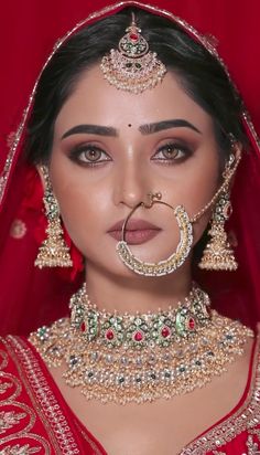 a woman in a red bridal outfit with jewelry on her neck and nose ring