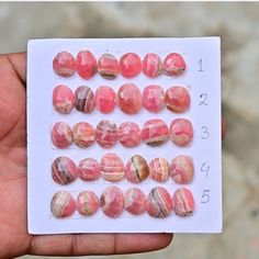 a hand holding a white card with red and pink marble beads on it's side