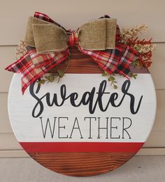 a wooden sign that says sweater weather on the side of a building with a bow