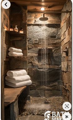 a bathroom with stone walls and a waterfall in the shower area that is surrounded by towels