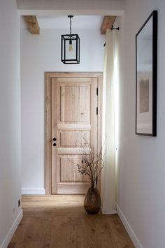 an empty hallway with a wooden door and vase on the floor