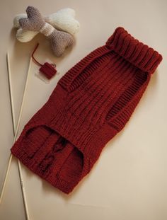 a knitted sweater and two knitting needles are on the table next to each other