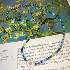 an open book with a necklace on top of it next to a tree and flowers