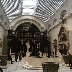 the inside of a building with statues and people standing around it in front of a skylight