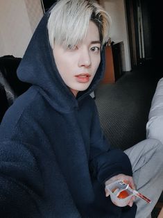 a person sitting on a couch with a toothbrush in their hand and wearing a blue hoodie