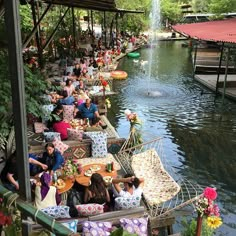 many people are sitting on boats in the water near a fountain and some tables with food