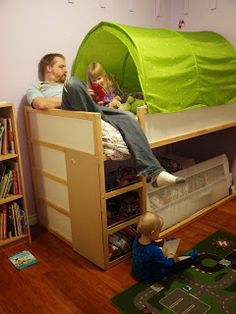 a man and child sitting on top of bunk beds in a room with bookshelves