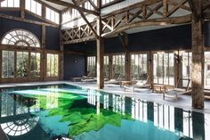 an indoor swimming pool surrounded by wooden beams and windows, with chairs around the edge